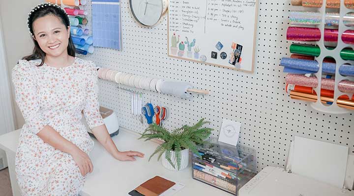 Young woman sitting on a white table in front of a DIY pegboard storage wall